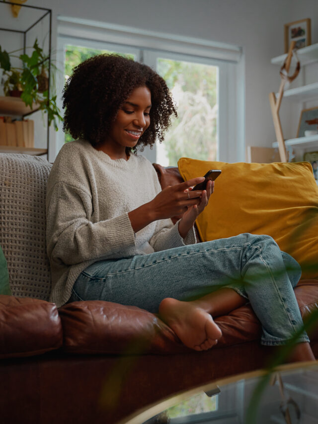 Stories Happy young african woman using mobile phone while sitting a couch at home